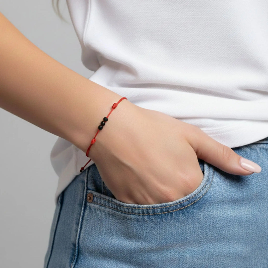 Person wearing a red string and black tourmaline beaded bracelet on a plain background