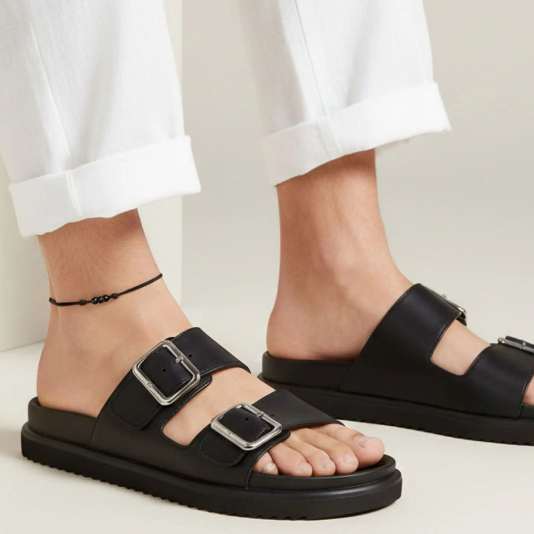 Black string anklet with three natural black tourmaline beads on a woman’s ankle, styled with black sandals with buckles worn by a person on a light background