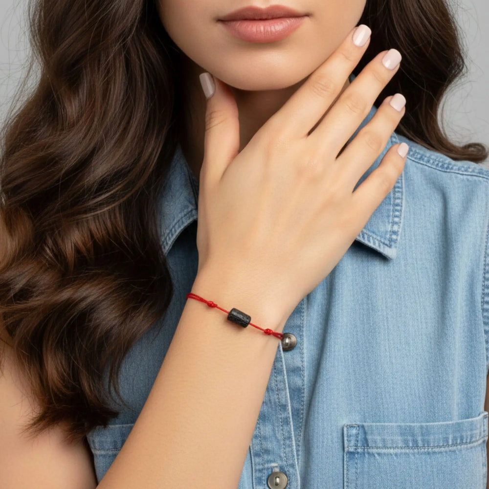 Woman wearing a red bracelet with black tourmaline beads on a gray background