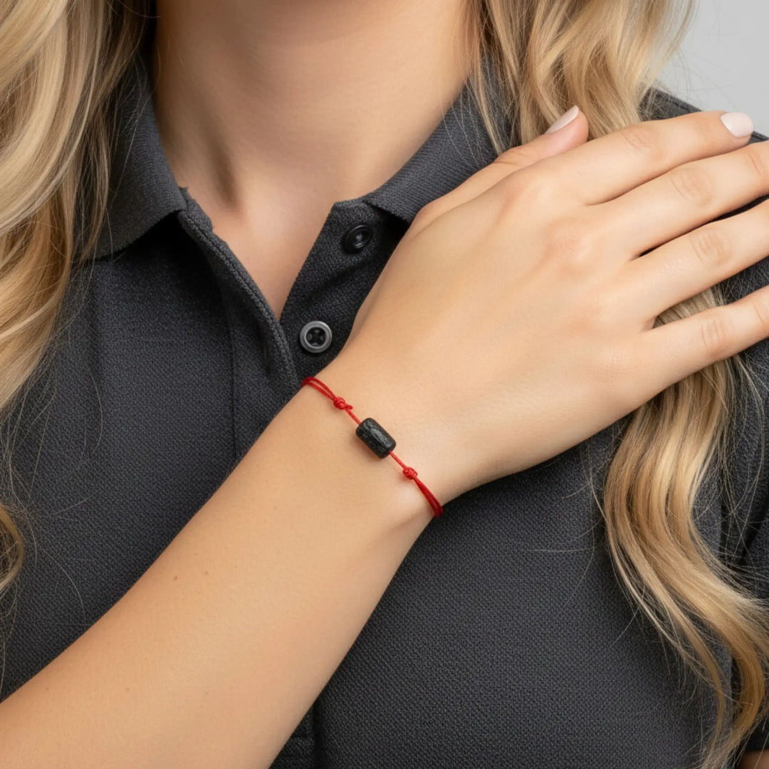 Person wearing a red bracelet with a black  torumaline bead on a gray background