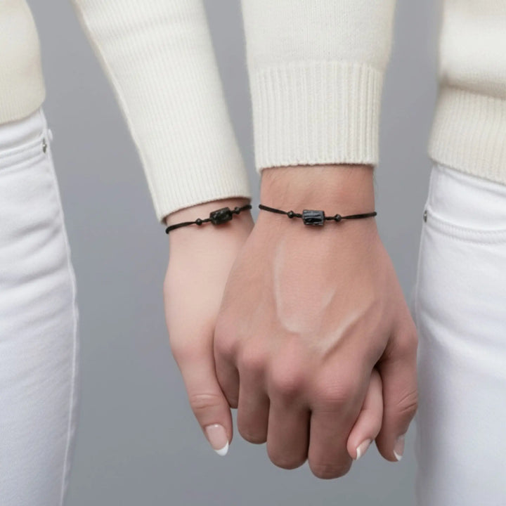 Two hands wearing matching raw black tourmaline bracelets on black cord (couple set).
