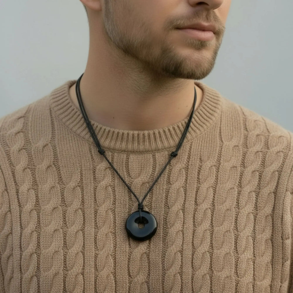 Man wearing a beige cable knit sweater with a black tourmaline necklace featuring a round pendant.