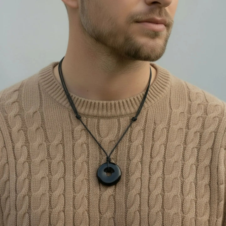 Man wearing a beige cable knit sweater with a black tourmaline necklace featuring a round pendant.