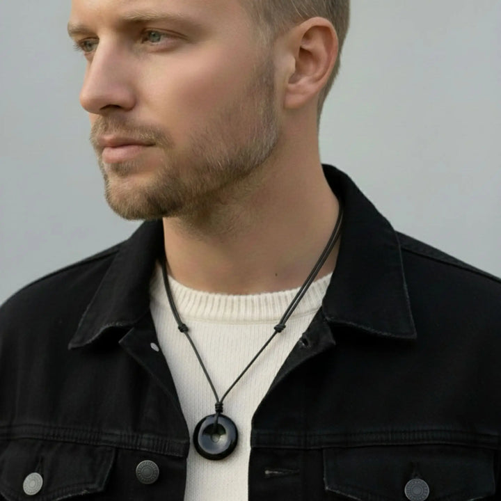 Man wearing a black tourmaline jacket and white shirt with a necklace against a gray background