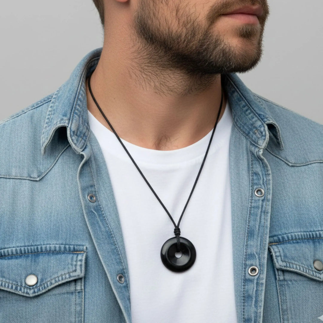 Man wearing a denim jacket and white shirt with a black tourmaline necklace featuring a round pendant.