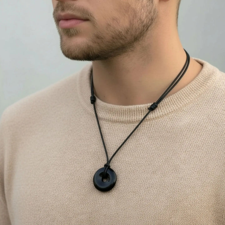 Man wearing a black tourmaline necklace with a round pendant against a neutral background
