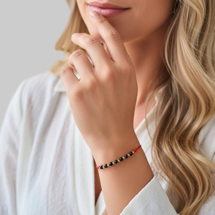 Close-up of a woman's hand wearing a black tourmaline solid gold beaded bracelet on a neutral background