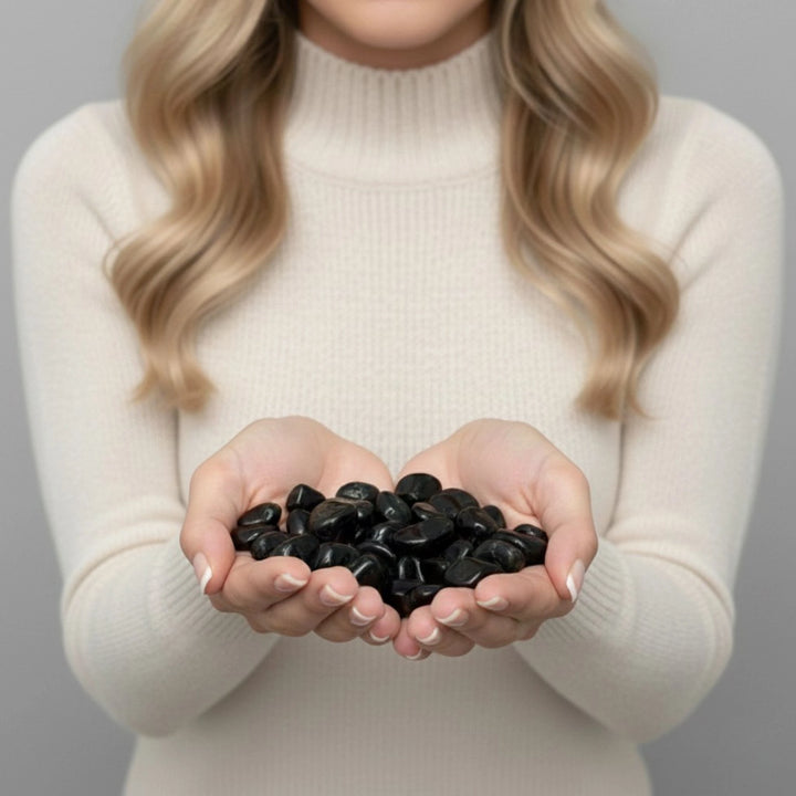 Person holding black tourmaline stones in their hands against a neutral background