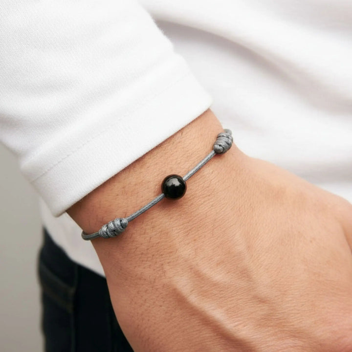 Bracelet with a black tourmaline bead and silver cord on a wrist against a white background