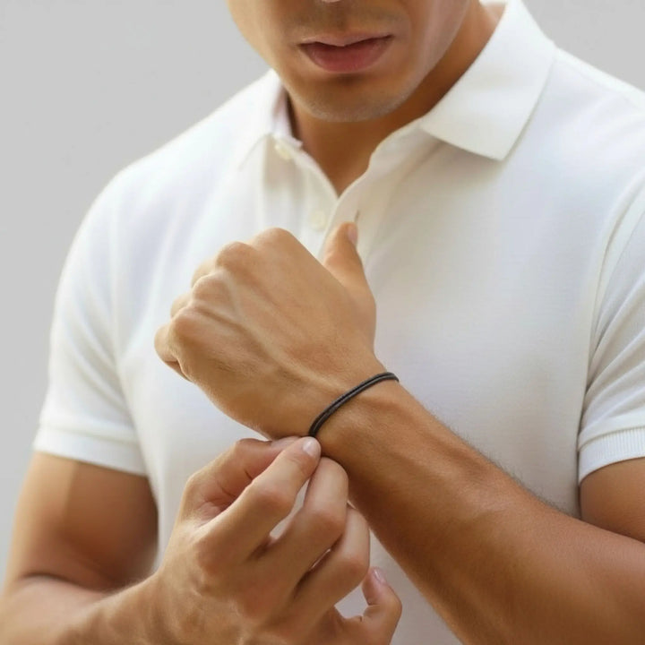 Man wearing a black bracelet on his wrist against a plain background