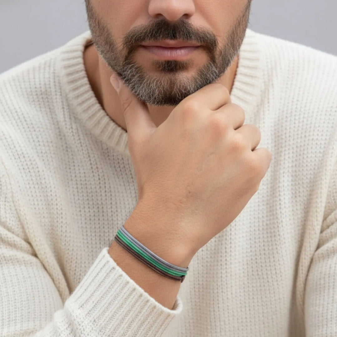 Man wearing a beige sweater with a bracelet on his wrist, against a gray background