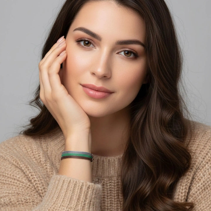 Woman with long brown hair wearing a beige sweater and a brown, green, and gray cord bracelet trio against a gray background