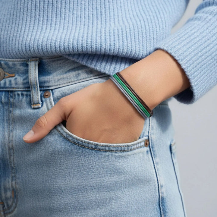 Person wearing a blue sweater and light blue jeans with a green and brown and grey bracelet on wrist.