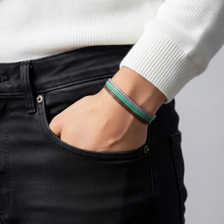 Person wearing a white sweater and black pants with a bronw green and gray bracelet on a plain background