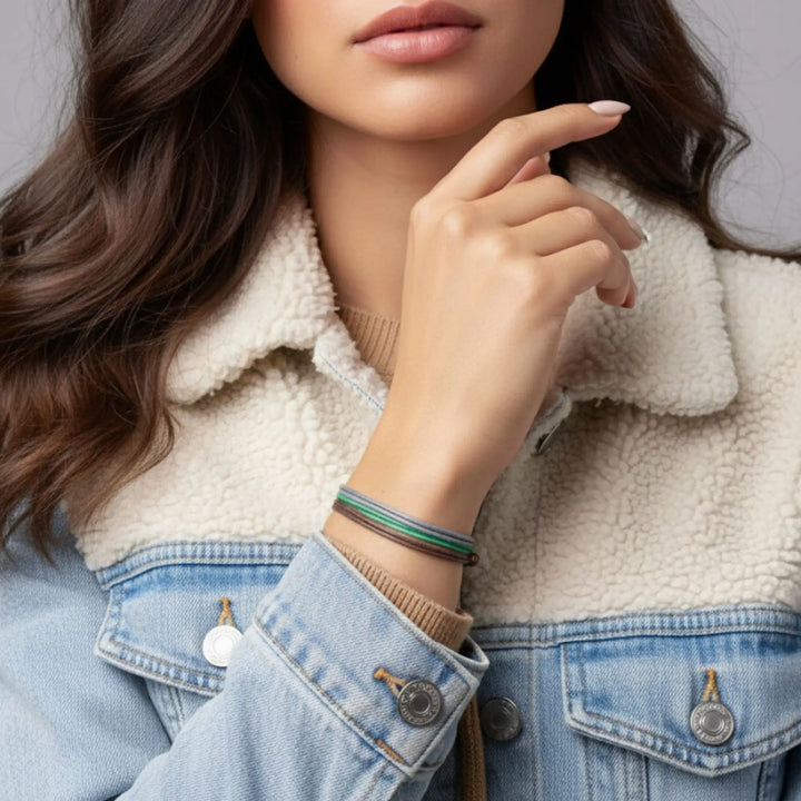 Close-up of a person wearing a denim jacket and white fleece-lined jacket with bracelets on a neutral background