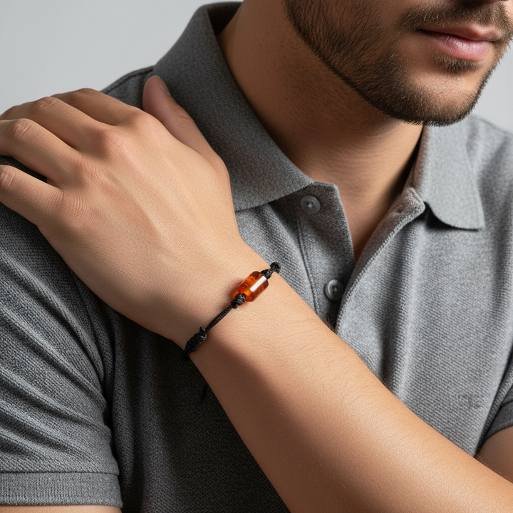 Man wearing carnelian cylinder bead bracelet on black waxed cord, close-up of wrist.
