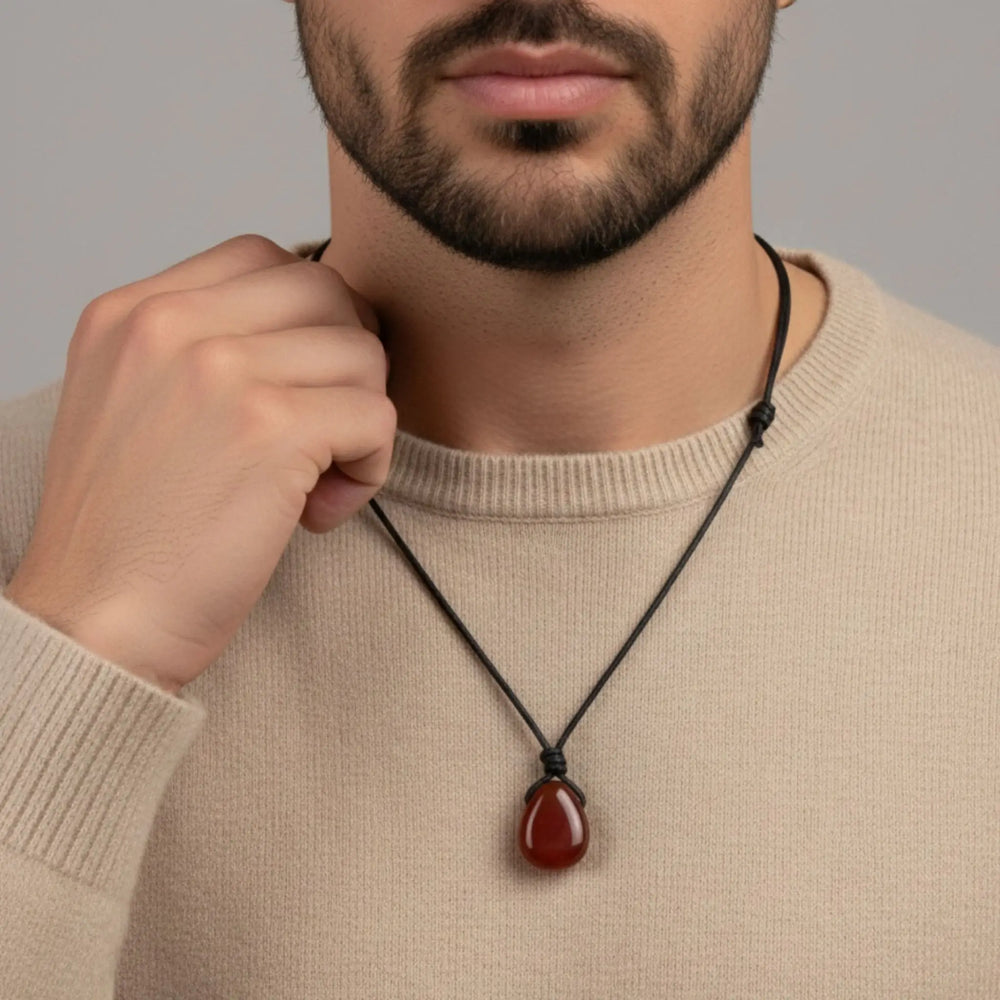 Man wearing a necklace with a red carnelians pendant against a neutral background