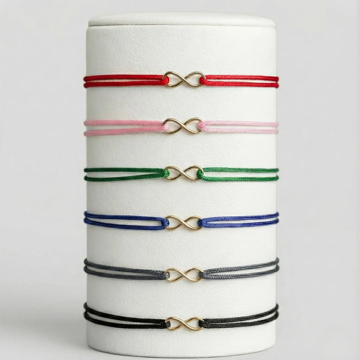 Set of colorful bracelets with infinity symbols on a white cylindrical stand.
