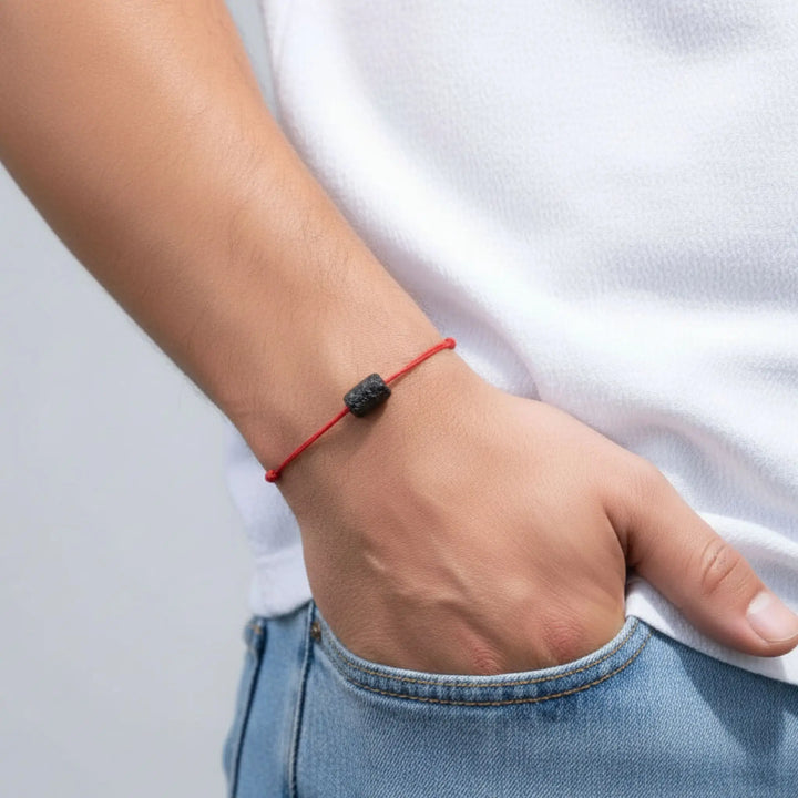 Person wearing a red bracelet with a black tourmaline bead on a plain background