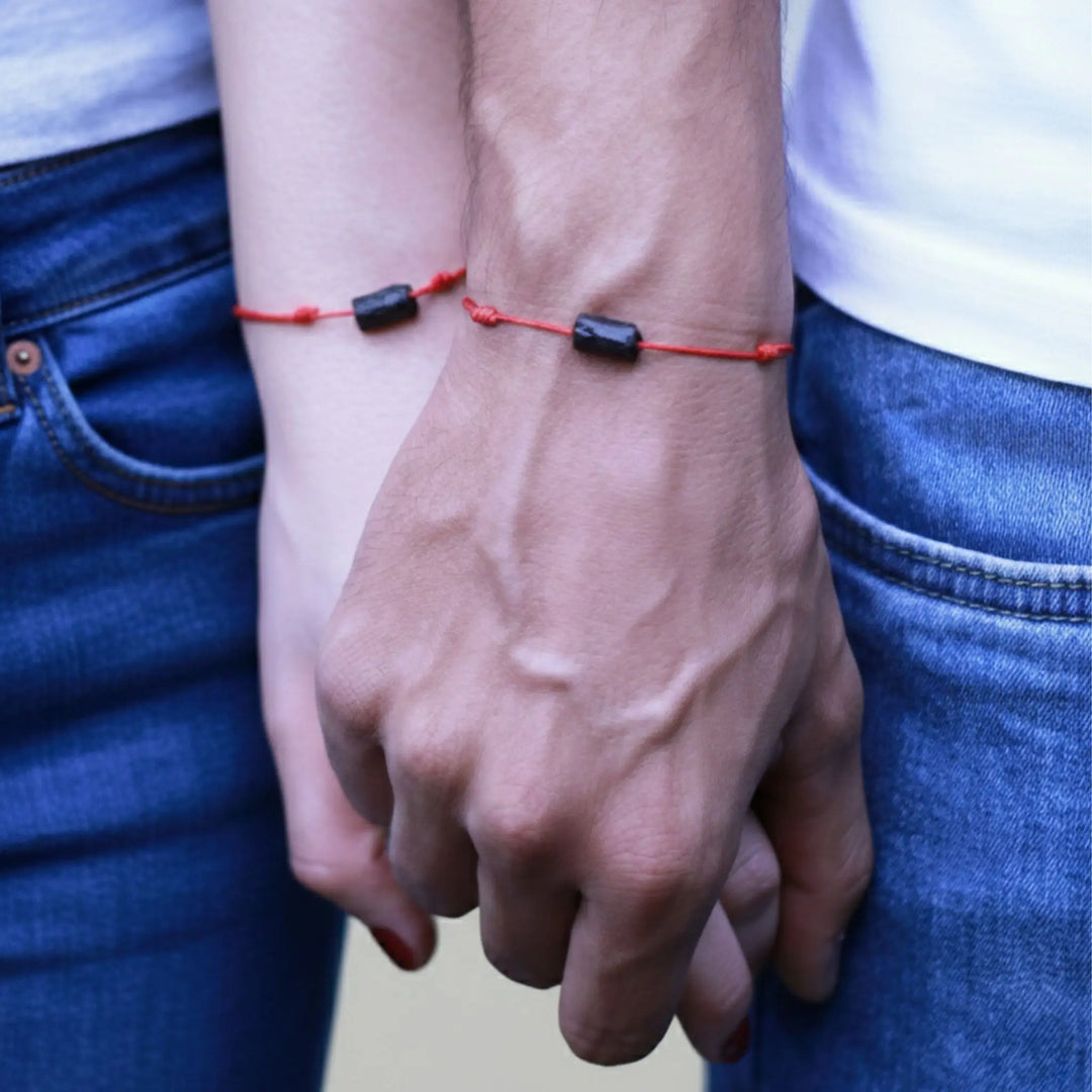 Two hands holding each other with a red bracelet featuring black tourmaline beads.