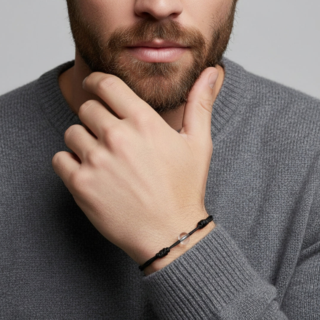 Man wearing a black cord bracelet with crystal quartz beads on his wrist.
