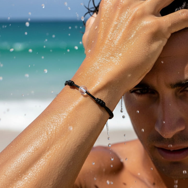 Man wearing a black cord bracelet with crystal quartz beads on his wrist near the ocean.
