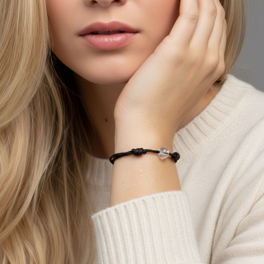 Woman wearing a black cord bracelet with crystal quartz beads on her wrist.
