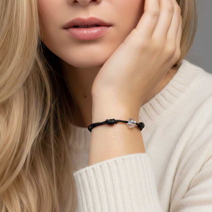 Woman wearing a black cord bracelet with crystal quartz beads on her wrist.

