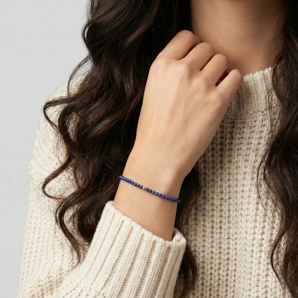 Person wearing a blue lapis lazuli beaded bracelet on a plain background