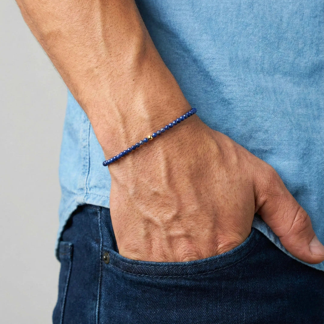 Person wearing a blue lapis lazuli beaded bracelet on a plain background