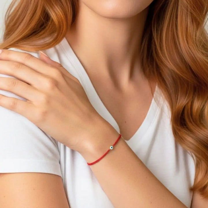 Woman wearing a red bracelet with a small gold evil eye bead on a white background
