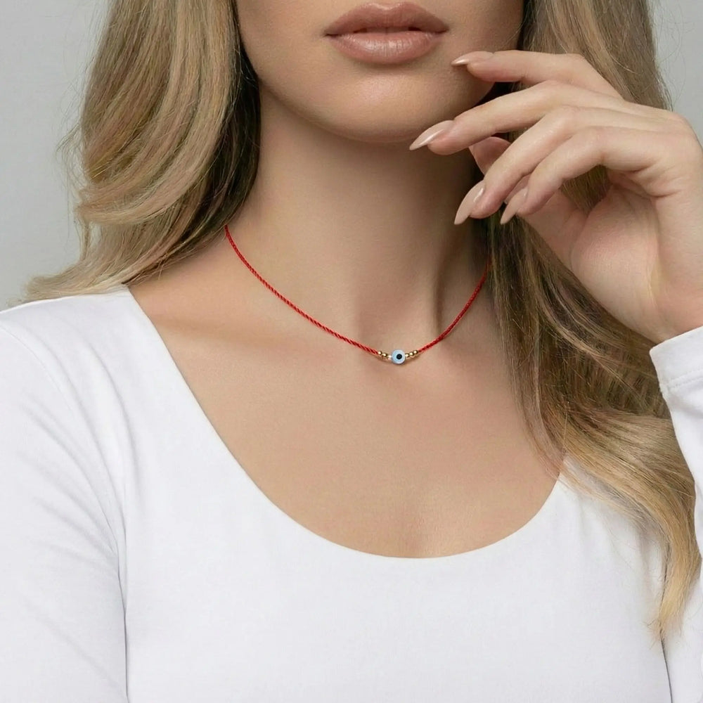 Woman wearing a red necklace with a small evil eye pendant against a neutral background