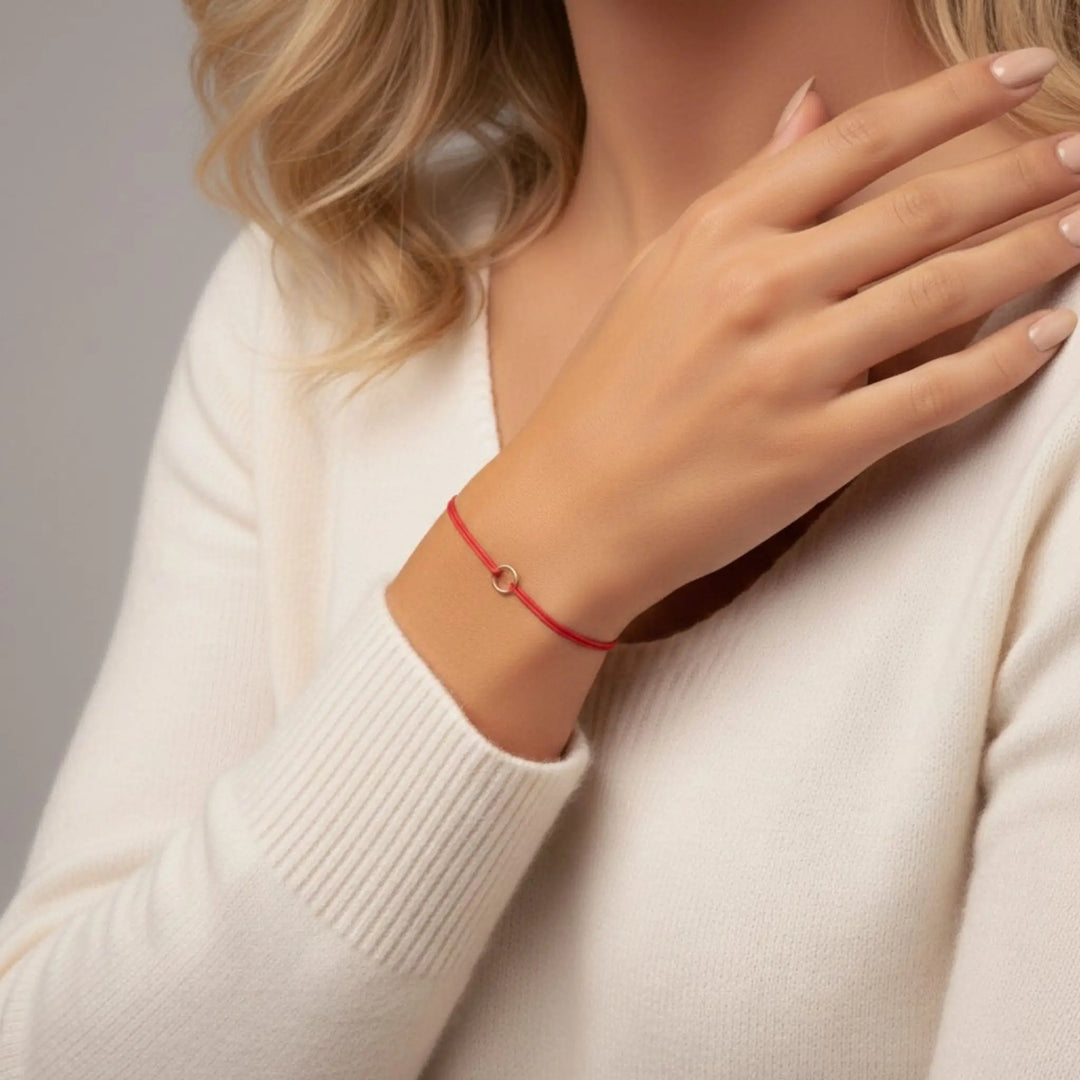 Person wearing a red gold bracelet on a neutral background