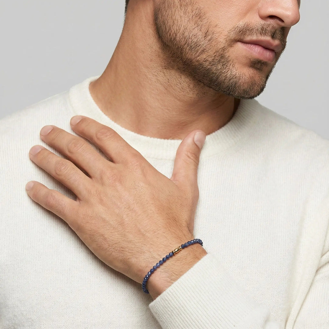 Man wearing a blue sapphire beaded bracelet on his wrist against a neutral background