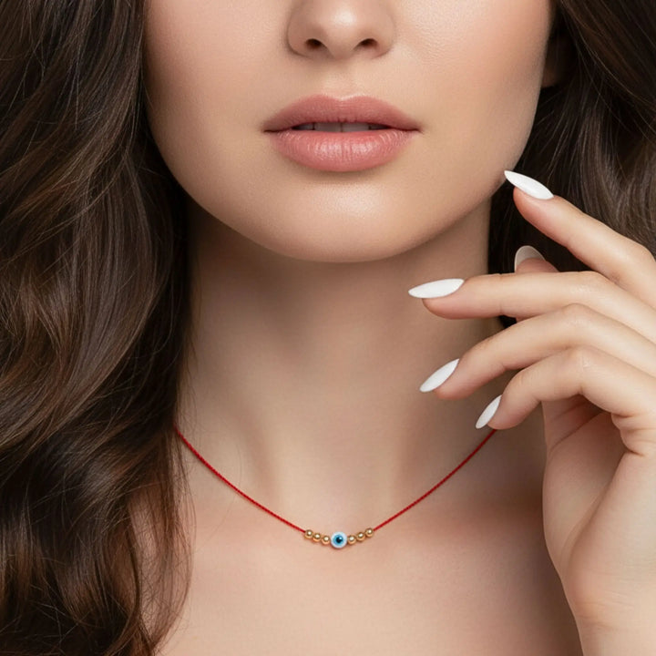 Close-up of a woman wearing a red evil eye necklace with a blue eye pendant.