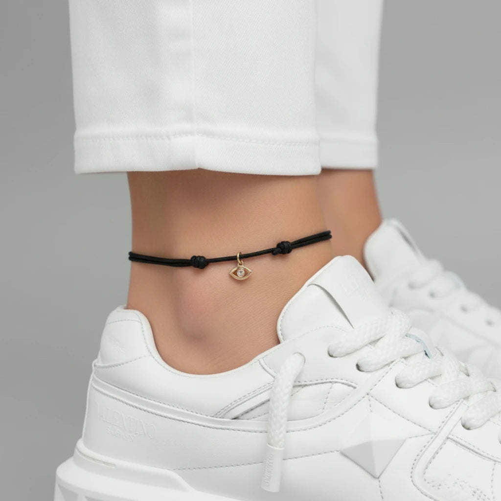 Red anklet with a gold charm on a person's ankle, wearing white sneakers and pants.