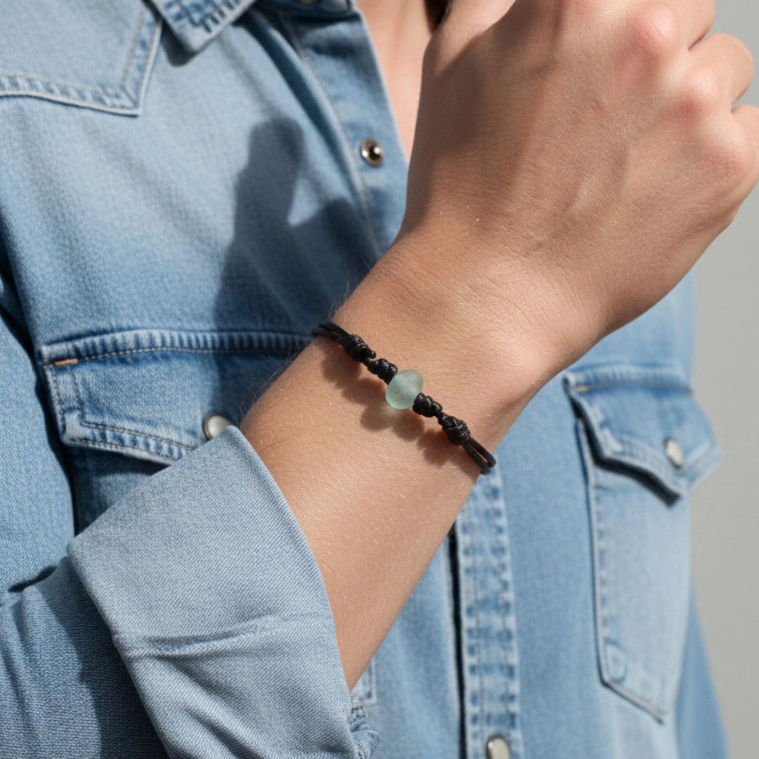 Person wearing a glass bracelet on a light blue denim jacket background