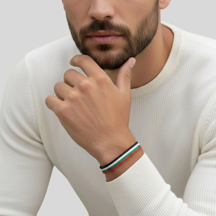 Man wearing a white sweater with a close-up of his hand and wrist showing a  emirates flag cord bracelet.  