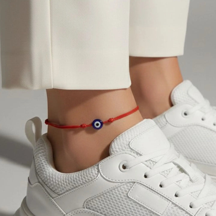 Person wearing a red anklet with a blue eye charm on a white background