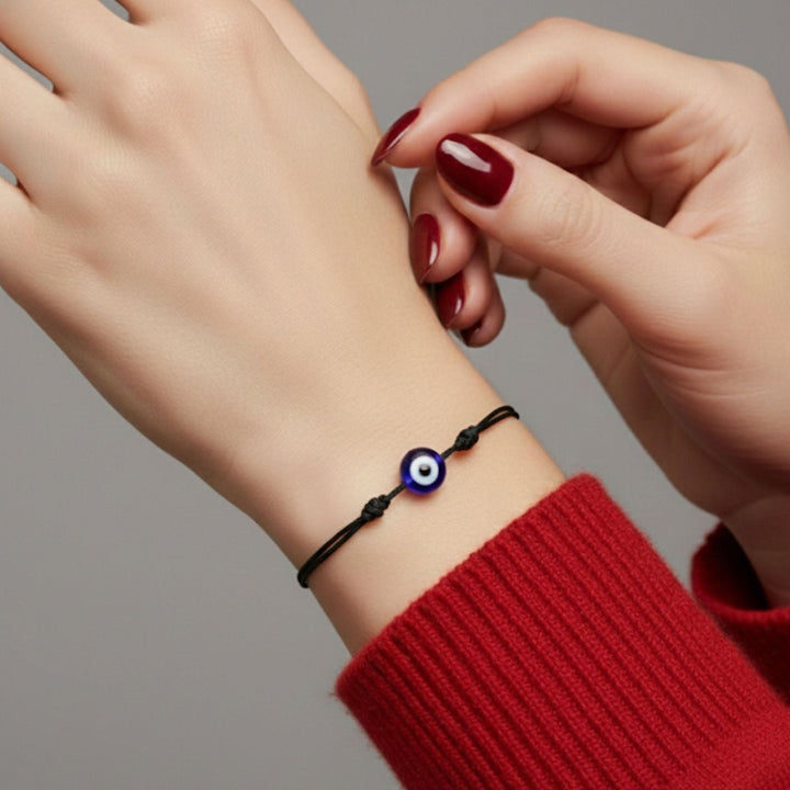 Hand wearing a bracelet with an eye charm on a neutral background