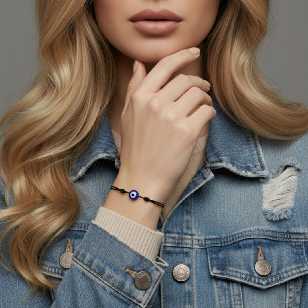Close-up of a person wearing a denim jacket with a hand resting on their chin, wearing a blue and black bracelet.