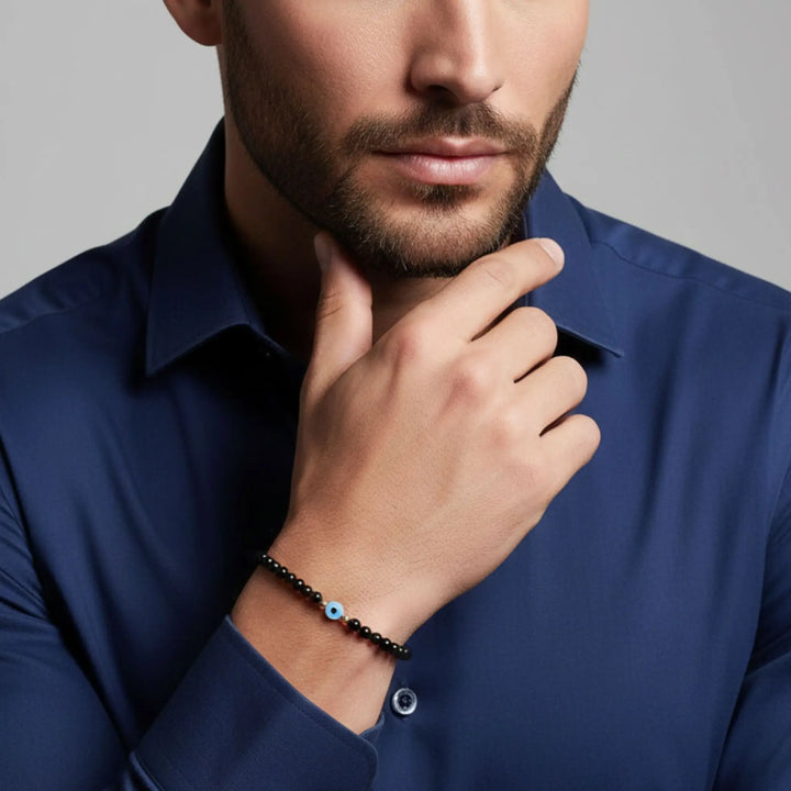 Man wearing a blue shirt with a close-up of his hand and evil eye black tourmaline bracelet on a gray background