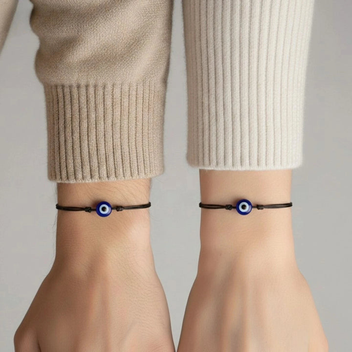 Two wrists wearing black bracelets with blue evil eye designs against a neutral background.