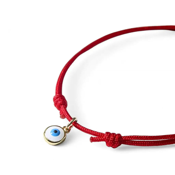 Red bracelet with a gold blue evil eye charm on a white background