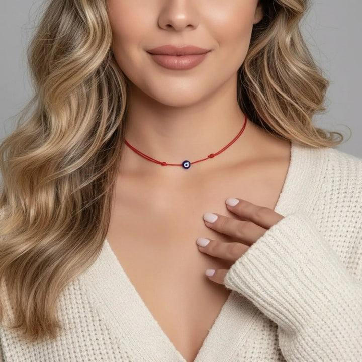 Woman wearing a red necklace with a blue evil eye pendant against a neutral background