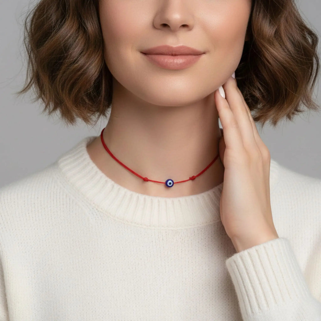 Woman wearing a red necklace with a blue evil eye pendant on a neutral background