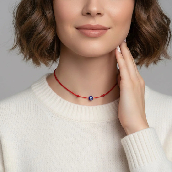 Woman wearing a red necklace with a blue evil eye pendant on a neutral background