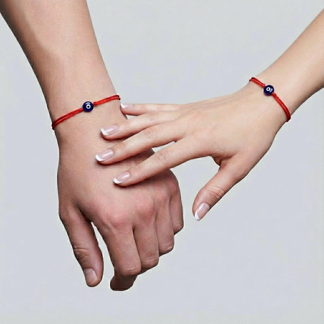 Two hands wearing red evil eye bracelets on a light gray background