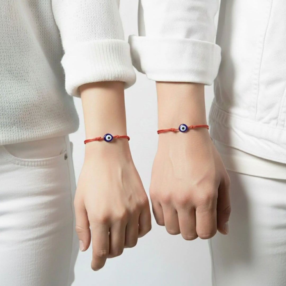 Two hands wearing red bracelets with blue evil eye symbols on a plain background