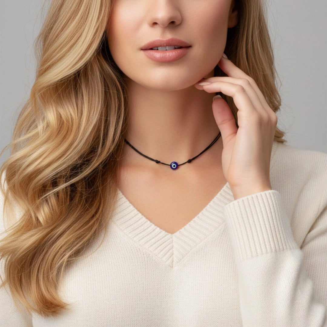 Woman wearing a black necklace with a blue evil eye pendant against a neutral background